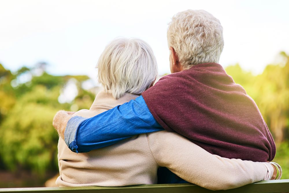 Senior couple hugging sitting on a bench, taken from their back