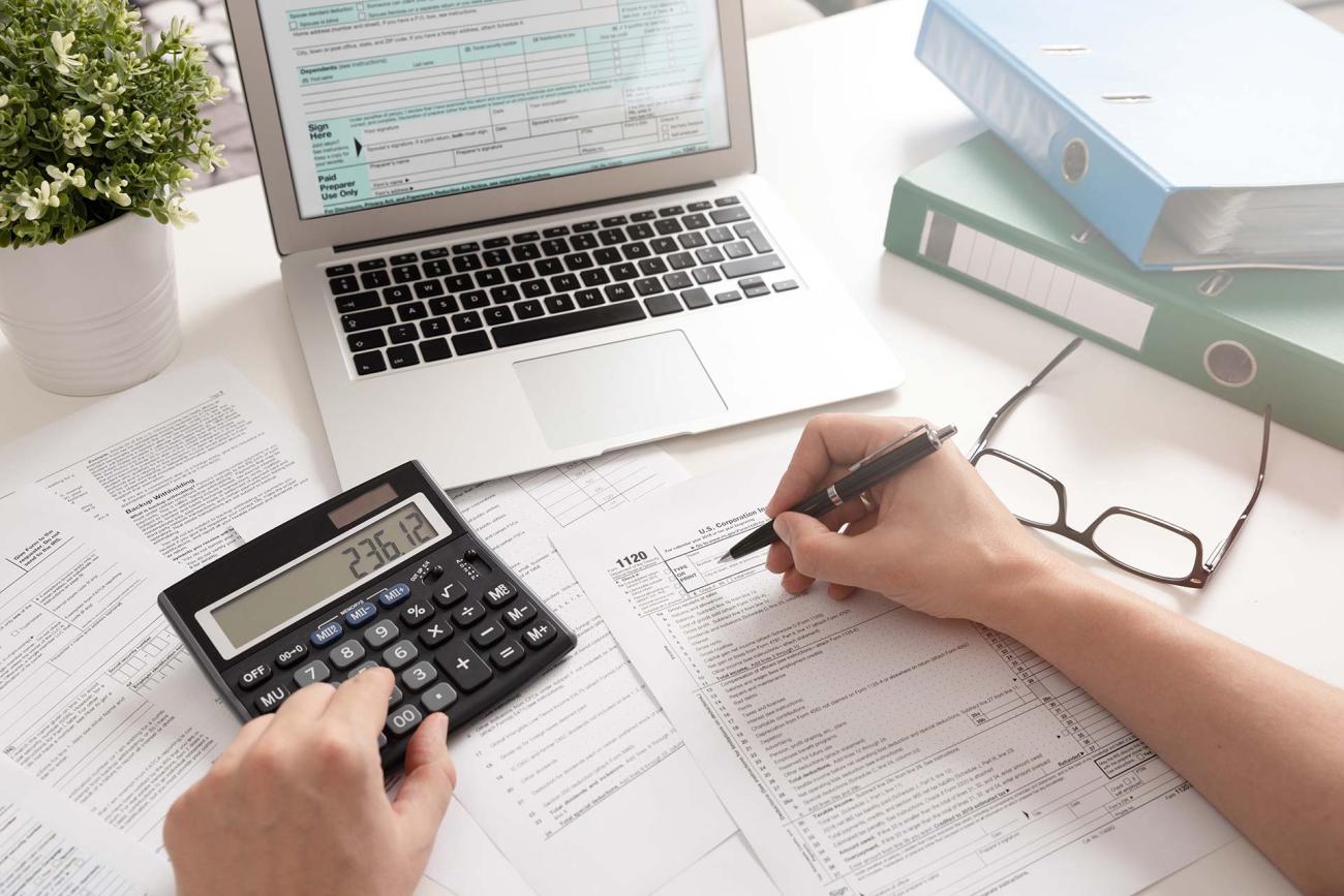 Person filling out a tax form with a laptop opened in front of them